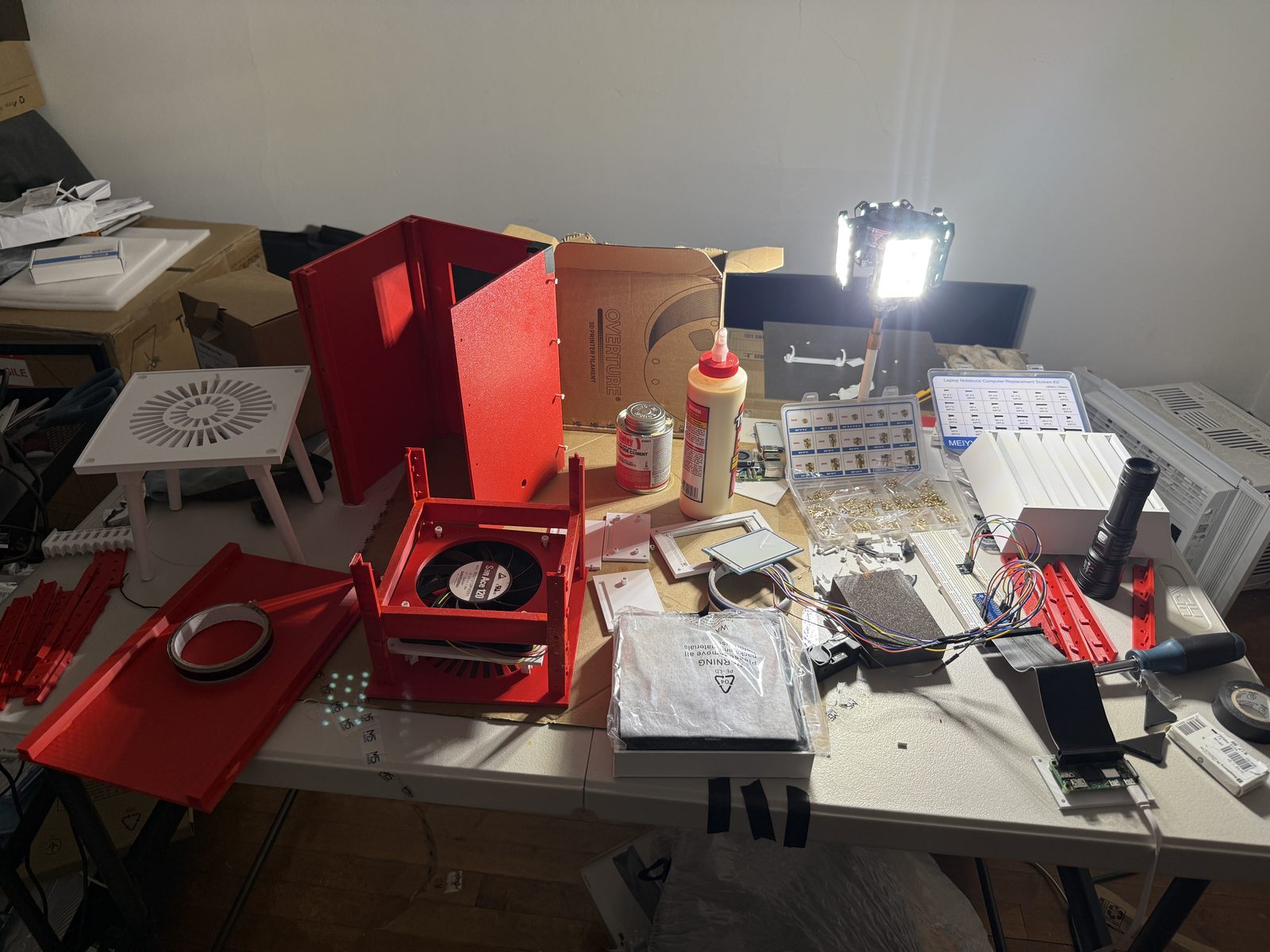 Linden Run A prototype on the workshop bench — red 3D-printed frame and panels, the e-paper display face, glue, and tools under a work light.