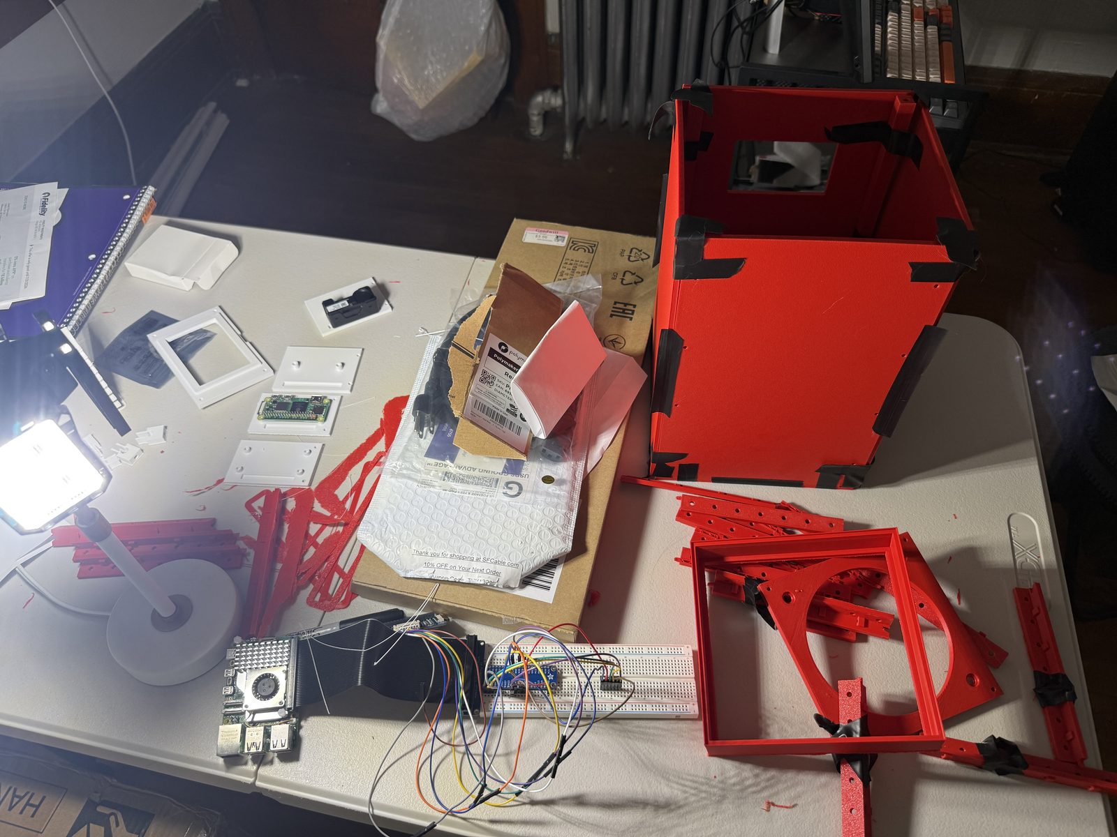Linden electronics on the bench — a breadboard wired with jumper leads, e-paper display modules, and red 3D-printed frame parts.