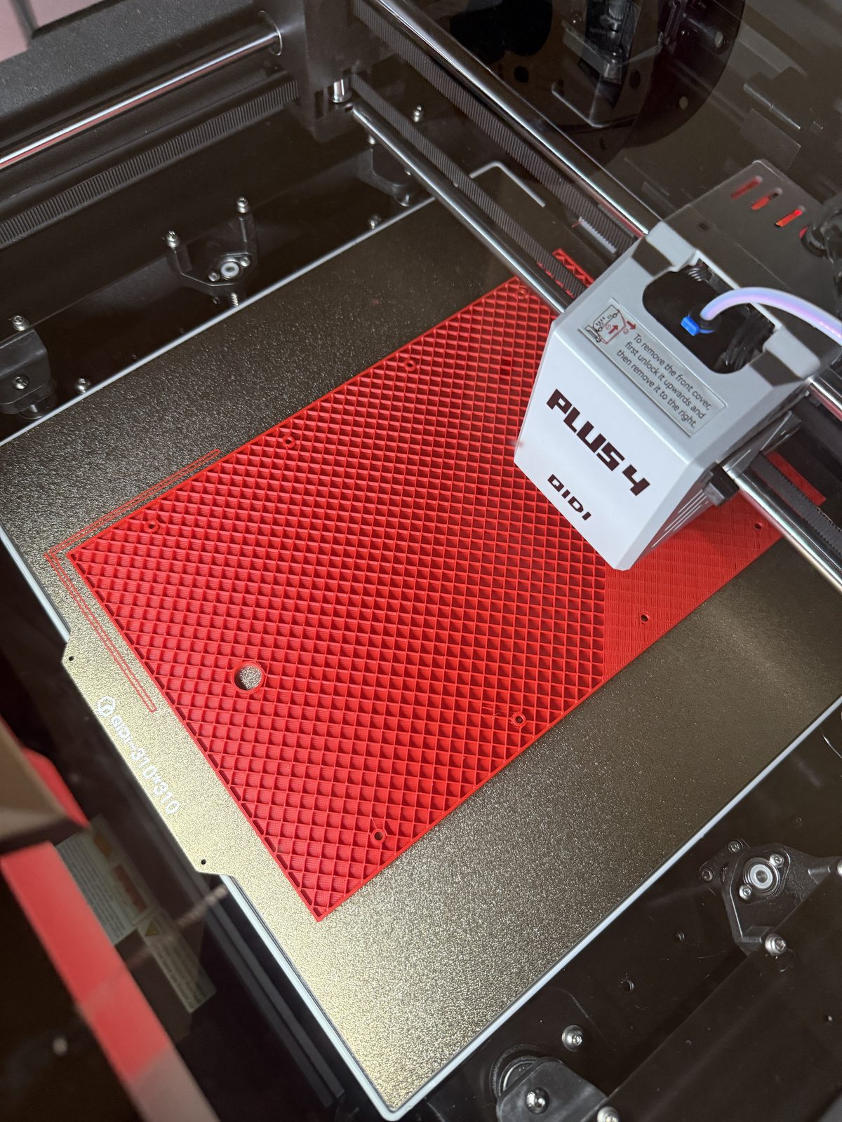 A red enclosure panel printing on a Qidi Plus 4 3D printer bed.